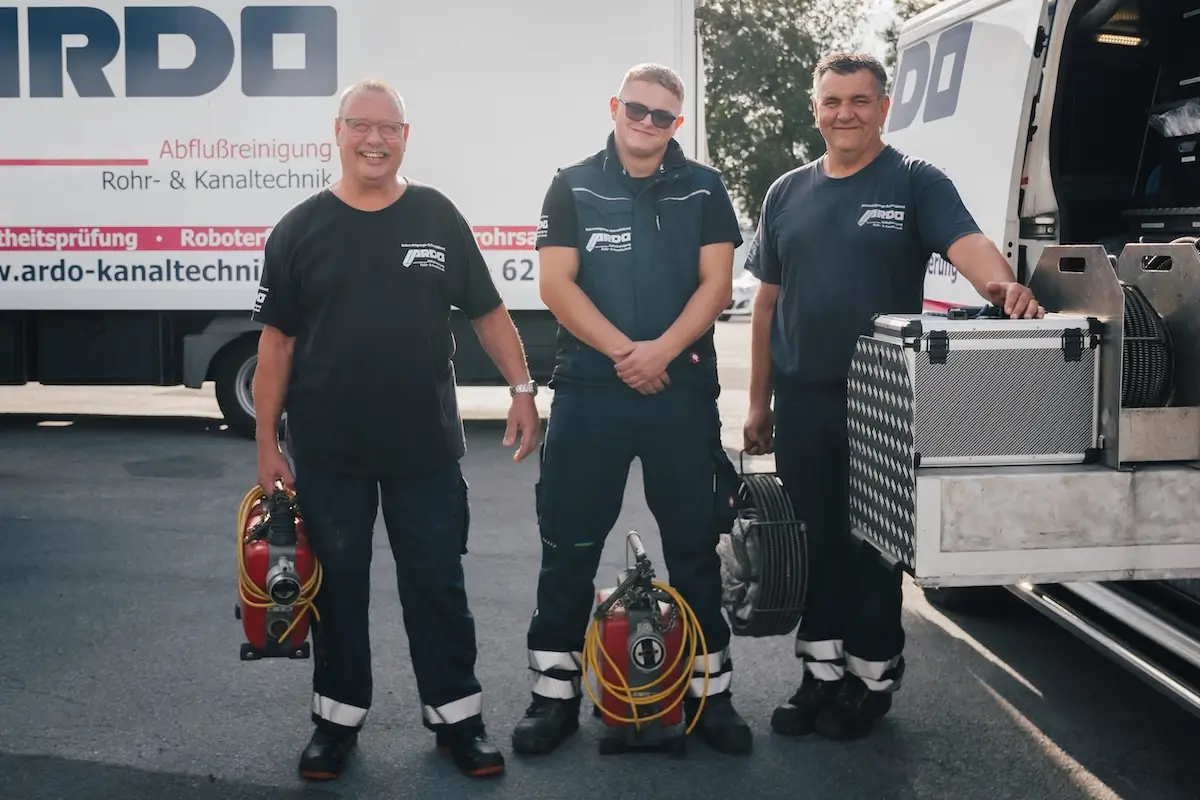 Drei Mitarbeiter des Unternehmens stehen an einem Einsatzfahrzeug